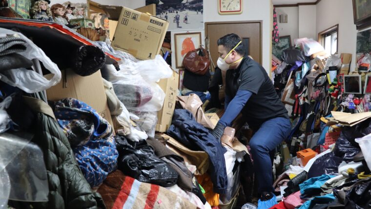 服や雑貨が積みあがった部屋の中で自社スタッフが佇んでいる様子