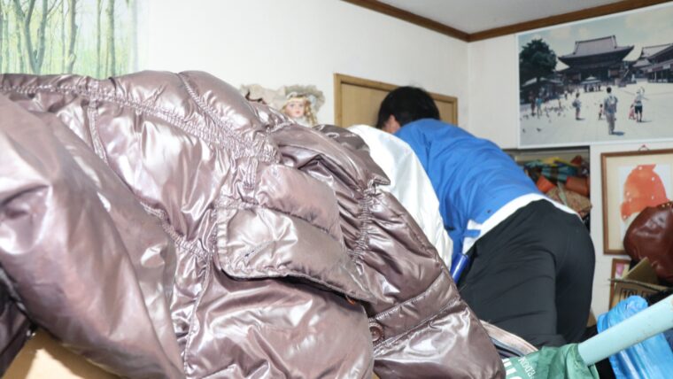 物が積まれた部屋の奥にいる自社スタッフ
